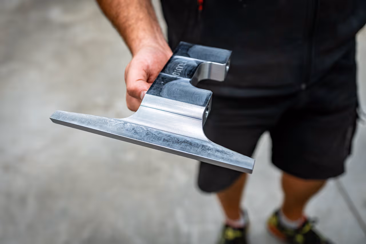 Ruka drží obrobený kovový díl s lesklým frézovaným povrchem
